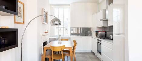 A modern kitchen with white cabinets, a dining table with chairs, and a pendant light.