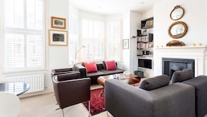 Ein modernes Wohnzimmer mit einer Couch, Sesseln, einem Couchtisch, einem Kamin und einem Bücherregal.