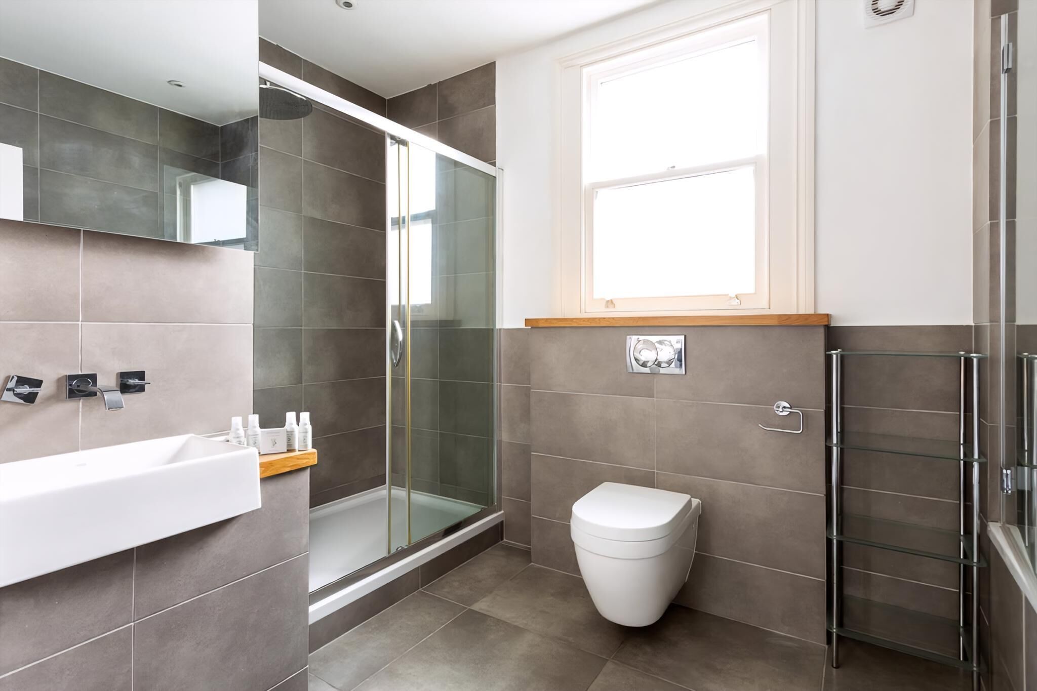 A modern bathroom with a glass shower enclosure, a white toilet, and a sink with a wooden shelf.