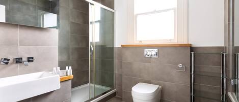 A modern bathroom with a glass shower enclosure, a white toilet, and a sink with a wooden shelf.