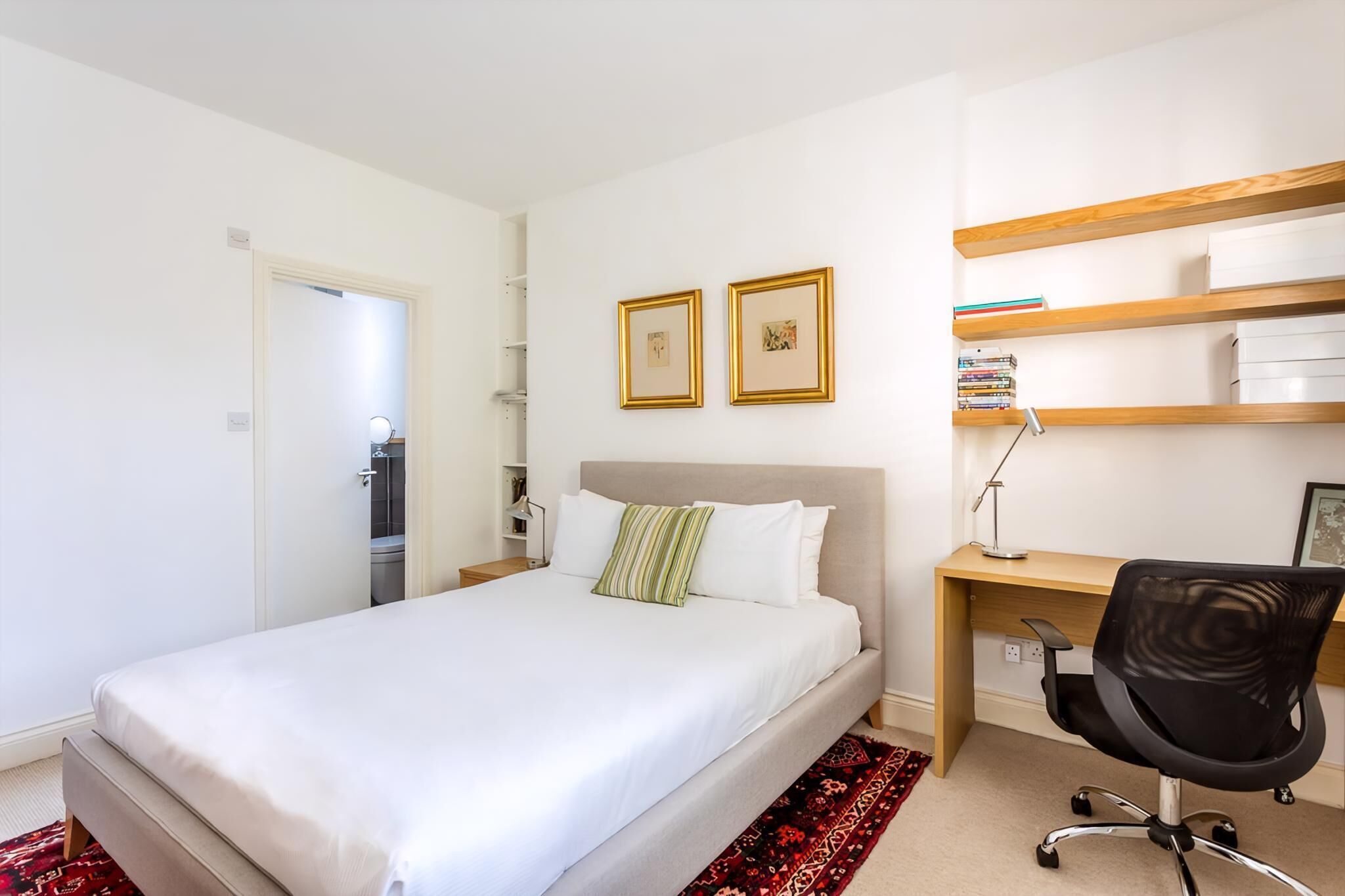 A bedroom with a bed, a desk, and two framed pictures on the wall.