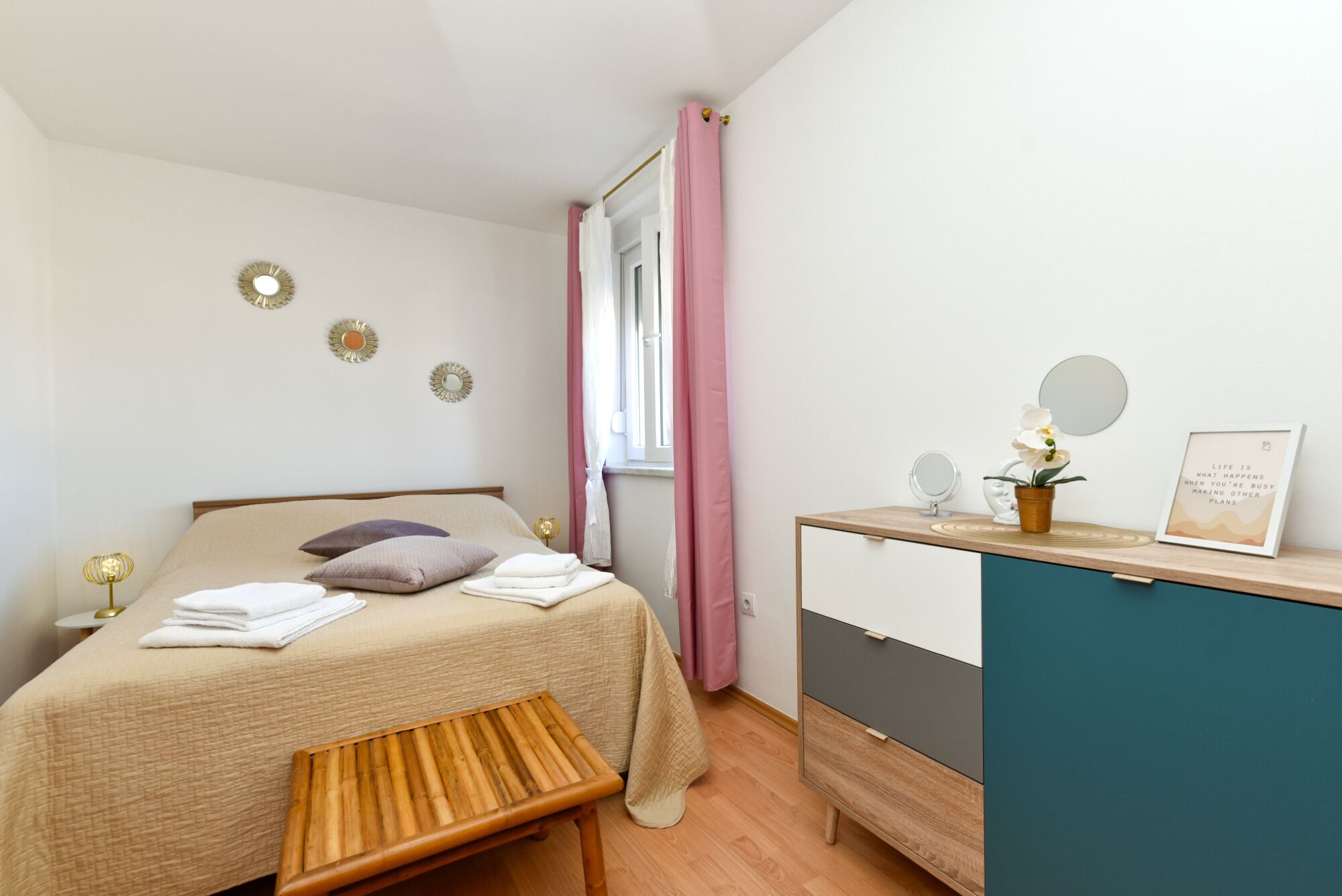 Un dormitorio con cama, mesita de noche y escritorio con espejo y planta en maceta.