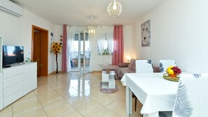 Una sala de estar moderna con un televisor de pantalla plana, una mesa de comedor con un frutero y un sofá.