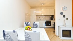 Una cocina moderna con armarios blancos, microondas y estufa. Hay un comedor con una mesa y sillas, y un pequeño adorno en la pared.