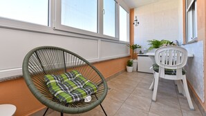 Un balcón con una silla de mimbre, una mesa de comedor con sillas y plantas en macetas.