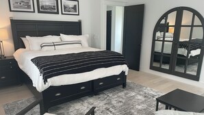 Un dormitorio moderno con una cama grande, cabecera de madera oscura, espejo con marco negro y vista a un balcón.