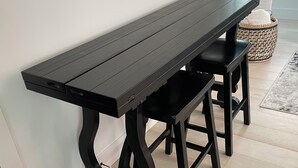 Un banco de madera negra con patas intrincadas, colocado frente a una pared blanca en una habitación con suelo de madera.