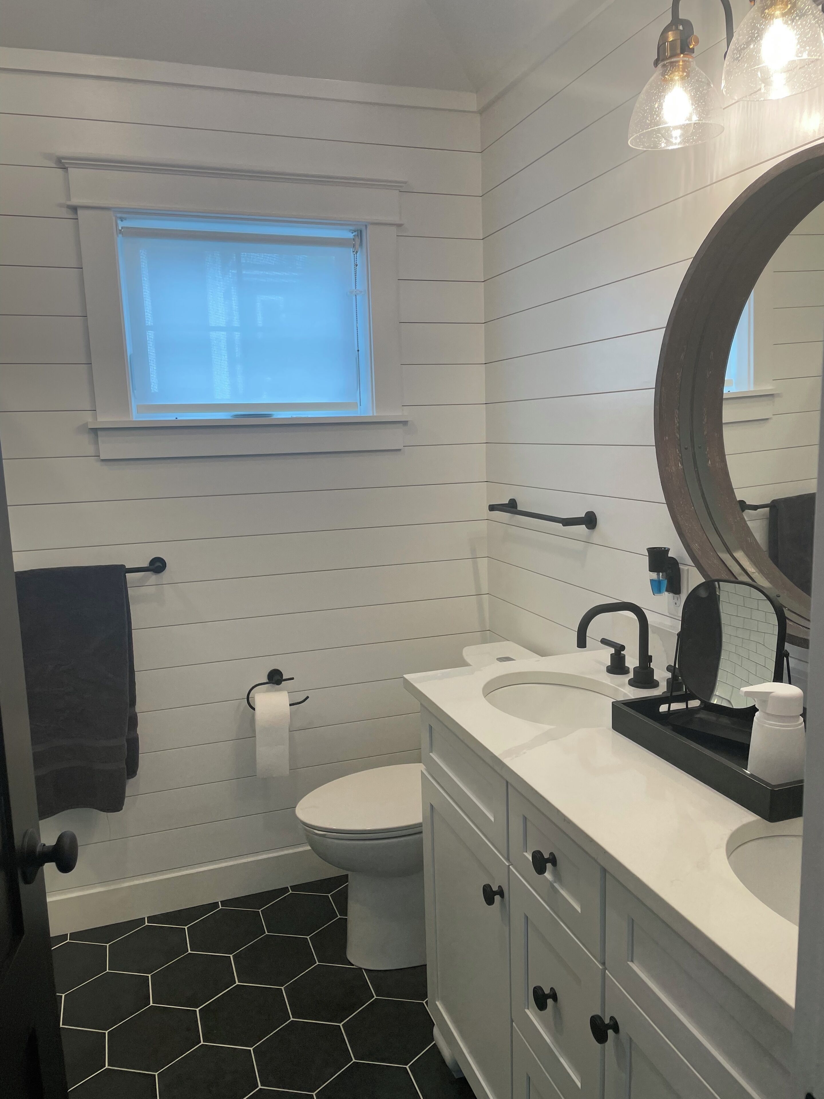 A bathroom with a white vanity, a round mirror, a toilet, and a window.