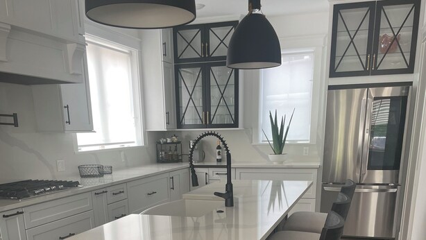 Una cocina moderna con una isla grande, armarios negros, electrodomésticos de acero inoxidable y una lámpara colgante.