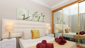 A hotel room with a large bed, two bedside tables with lamps, a large mirror, and artwork on the wall.