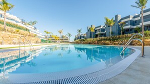 A swimming pool with clear blue water, surrounded by modern buildings and palm trees. - OASIS 325 penthouse with panoramic views (Estepona)