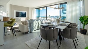 A modern living room with a dining area, large windows, a flat-screen TV, and a view of the city. - OASIS 325 penthouse with panoramic views (Estepona)