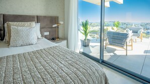 A modern hotel room with a large bed, a nightstand, and a view of the city through floor-to-ceiling windows. - OASIS 325 penthouse with panoramic views (Estepona)