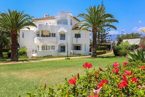 A white multi-story building with balconies, surrounded by well-maintained lawns and palm trees. - Ground-floor apartment in Elviria del Sol (Marbella)