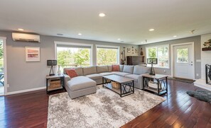 A modern living room with a sectional sofa, a piano, and a dining table.
