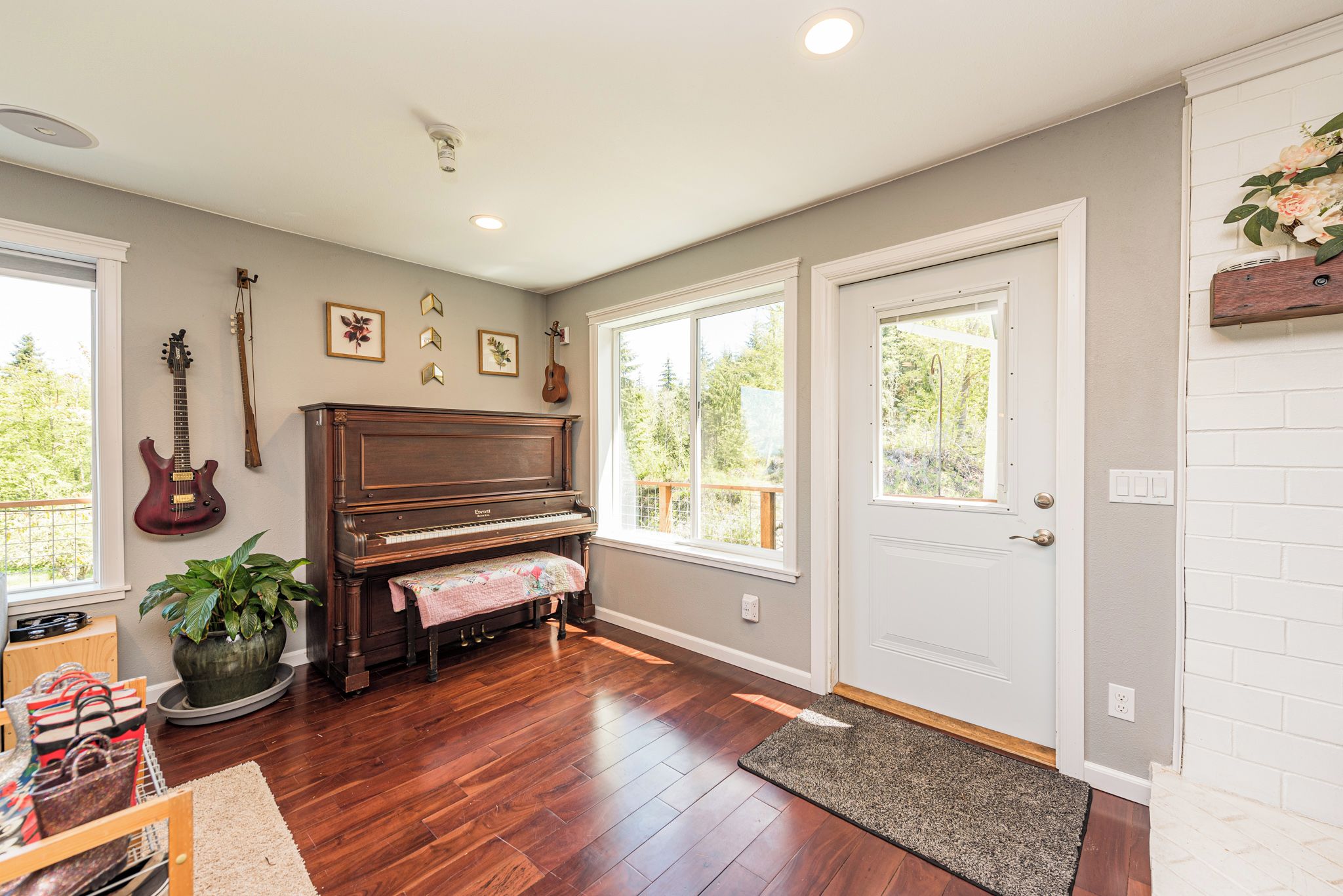 A room with a piano, a guitar, a potted plant, and a door with a window.