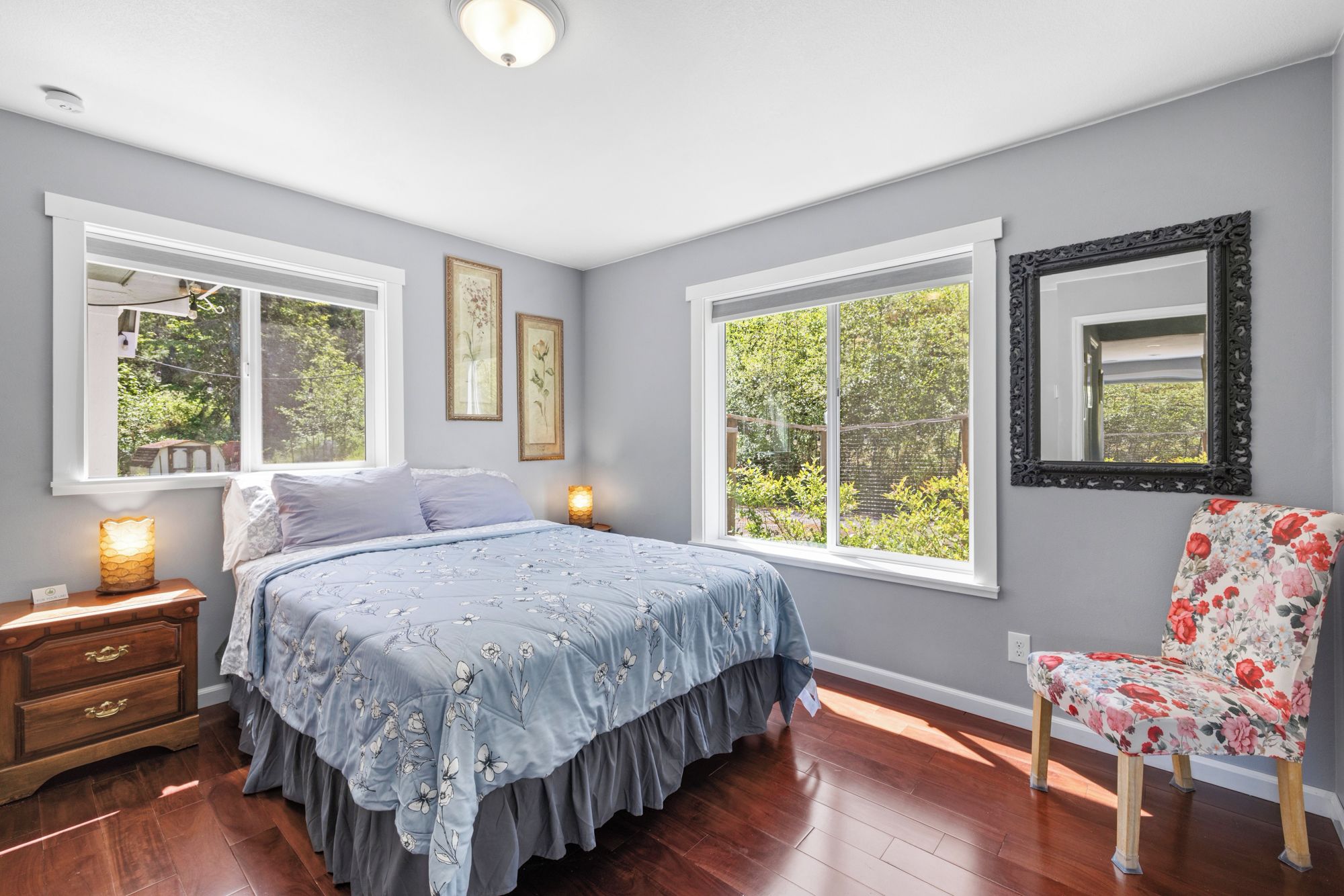 A bedroom with a bed, two windows, a chair, and a dresser.