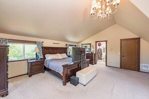 A bedroom with a large bed, a dresser, a vanity, a television, and a chandelier. - Private Home In the woods! (Sequim)