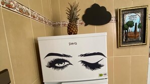 A kitchen with a refrigerator, a pineapple on top, and a framed picture on the wall.