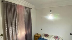 A bedroom with a bed, a nightstand, a ceiling fan, and a window with curtains.