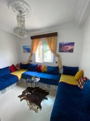 A living room with a blue sofa set, a small round table, and a chandelier. - Villa Issato (Tanger)