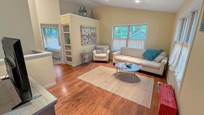 A living room with a sofa, coffee table, and TV stand. There is a rug on the floor and a window with curtains.