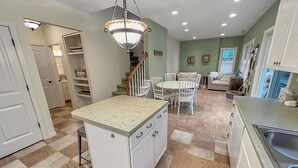 A kitchen with a central island, white cabinets, and a dining area with chairs.