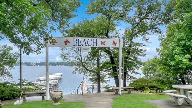 A beach entrance sign with a view of a lake and dock.