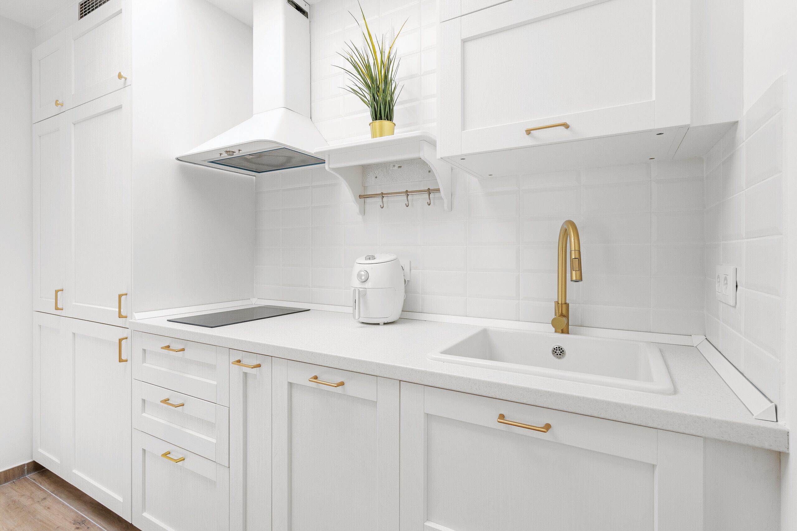 Una cocina moderna con armarios blancos, pomos dorados, horno integrado y grifo dorado.