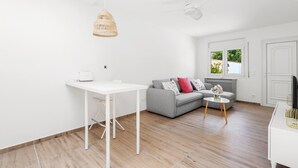 Ett modernt vardagsrum med ett vitt bord, en grå soffa och ett litet runt bord med blommor.