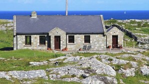 A stone house with a dark roof, a chimney, and a view of the sea. - Luxury Sea View Cottage: Ballyconneely, Clifden, Connemara, Galway. (Clifden)