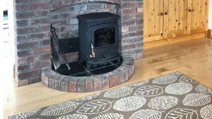 A living room with a brick fireplace, a television on a wooden cabinet, and a patterned rug. - Luxury Sea View Cottage: Ballyconneely, Clifden, Connemara, Galway. (Clifden)