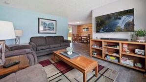 Ein Wohnzimmer mit einer Couch, einem Couchtisch und einem Fernseher. Es gibt einen Essbereich mit einem Tisch und Stühlen.