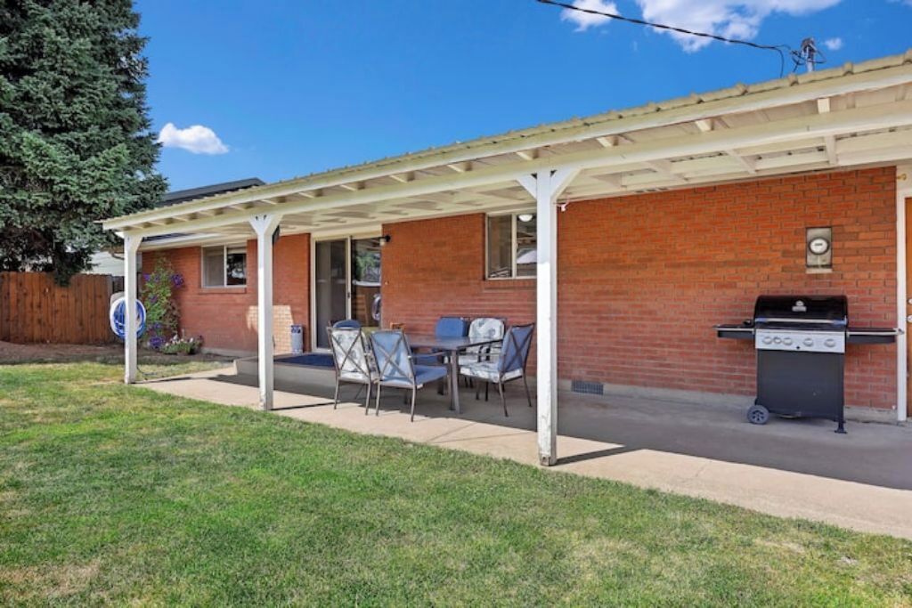A covered patio with a brick building, a grill, and outdoor seating.