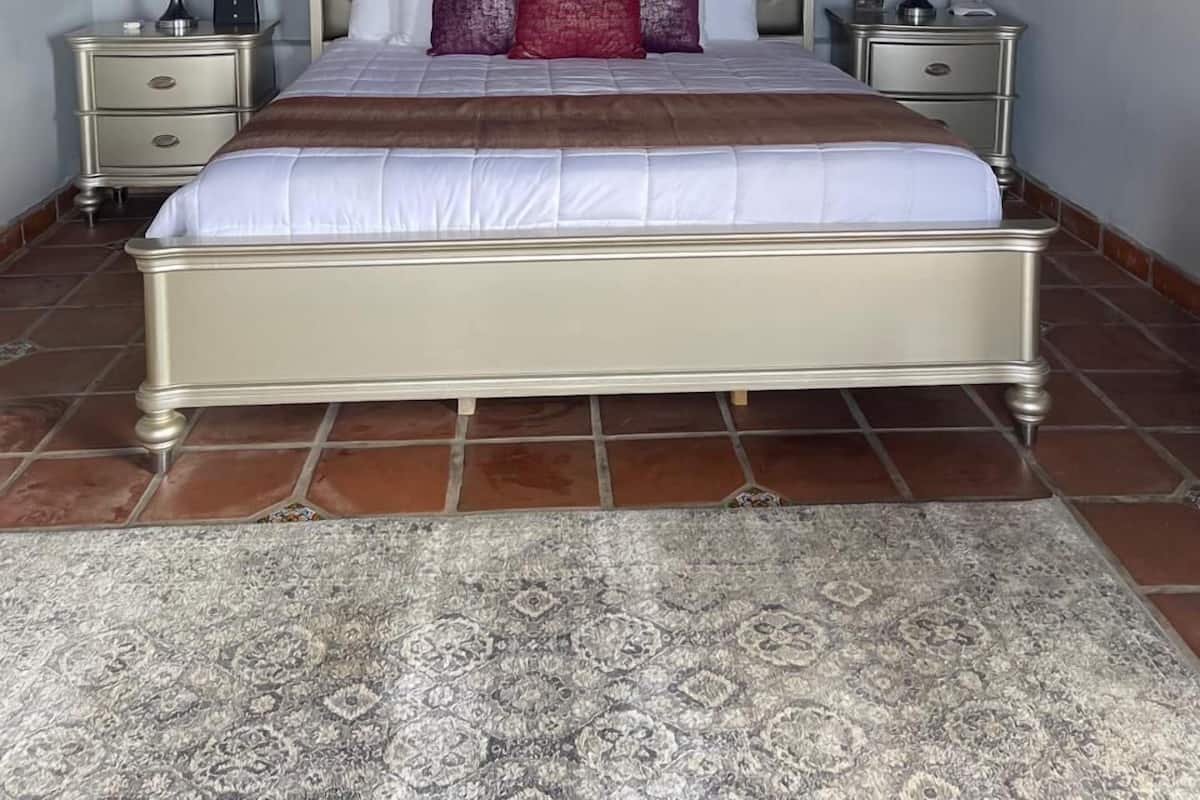 Une chambre à coucher avec un grand lit, deux tables de chevet, une tête de lit avec des lampes, un tableau au mur et un tapis à motifs.