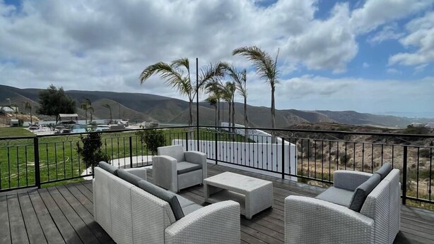 A deck with wicker furniture, a view of hills, and a cloudy sky. - Viñas del Castillo Hotel Boutique (Ensenada)