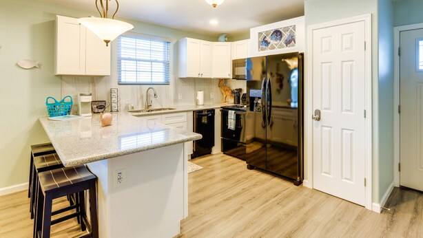 A modern kitchen with white cabinets, a central island with stools, a refrigerator, and a dishwasher. - Relax at Heron Bay Cottage in Rockport, Texas! (Rockport)