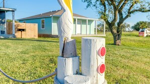 A rustic wooden sculpture with a painted figure, a wooden post with red circular elements, and a house in the background. - Relax at Heron Bay Cottage in Rockport, Texas! (Rockport)