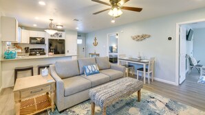 A modern living room with a sofa, a coffee table, and a dining area with a table and chairs. There is a kitchen area with a microwave and refrigerator. - Relax at Heron Bay Cottage in Rockport, Texas! (Rockport)