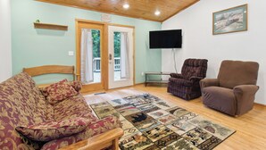Un salón acogedor con techo de madera, un sofá estampado, un sillón marrón y una alfombra acolchada.