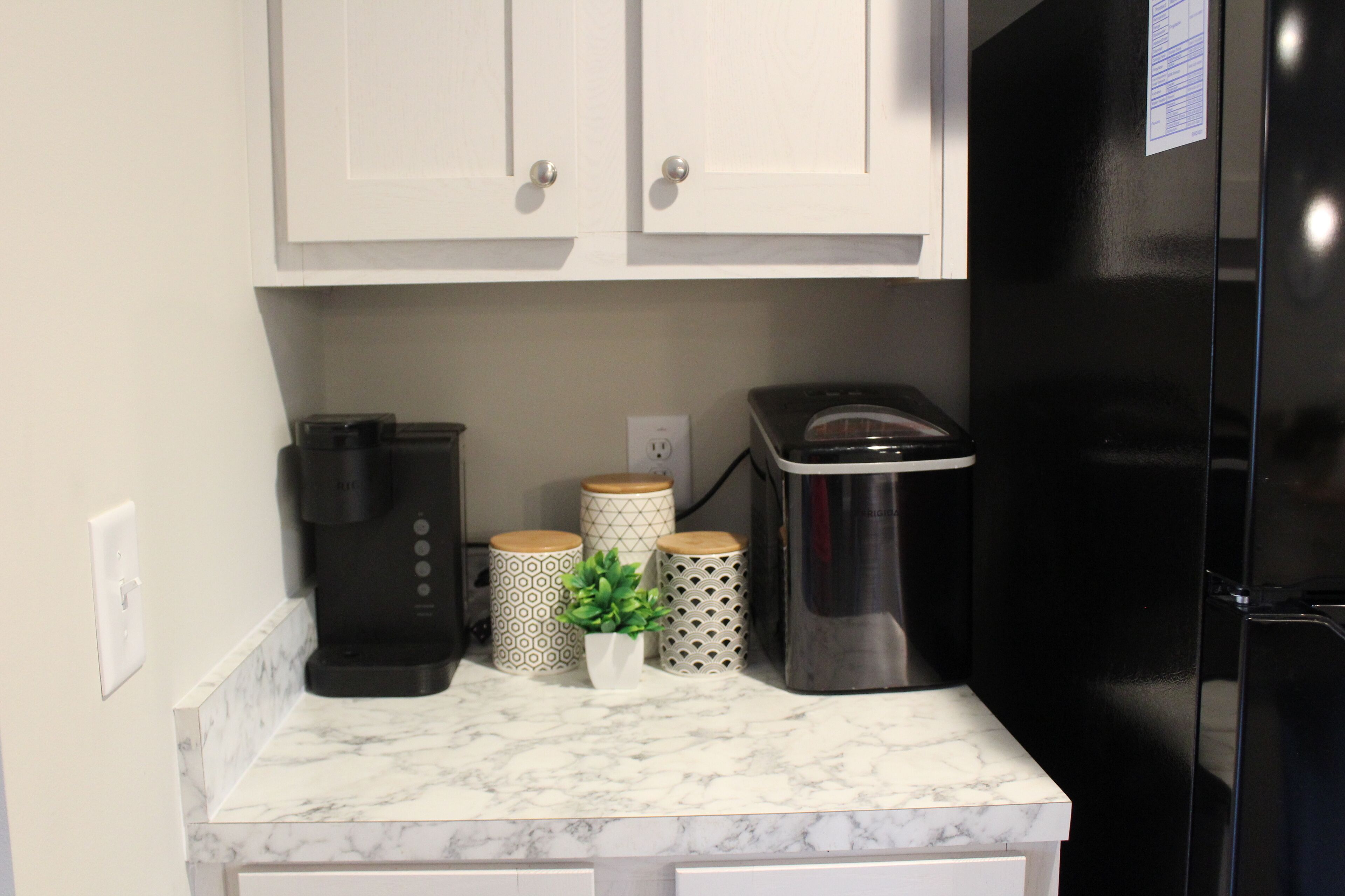 A kitchen with white cabinets, a black refrigerator, a coffee maker, and decorative containers.