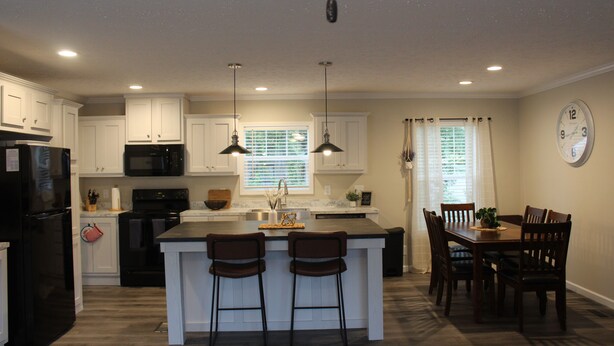 A modern kitchen with white cabinets, a black refrigerator, a microwave, and a sink. There are two bar stools and a dining table with chairs.
