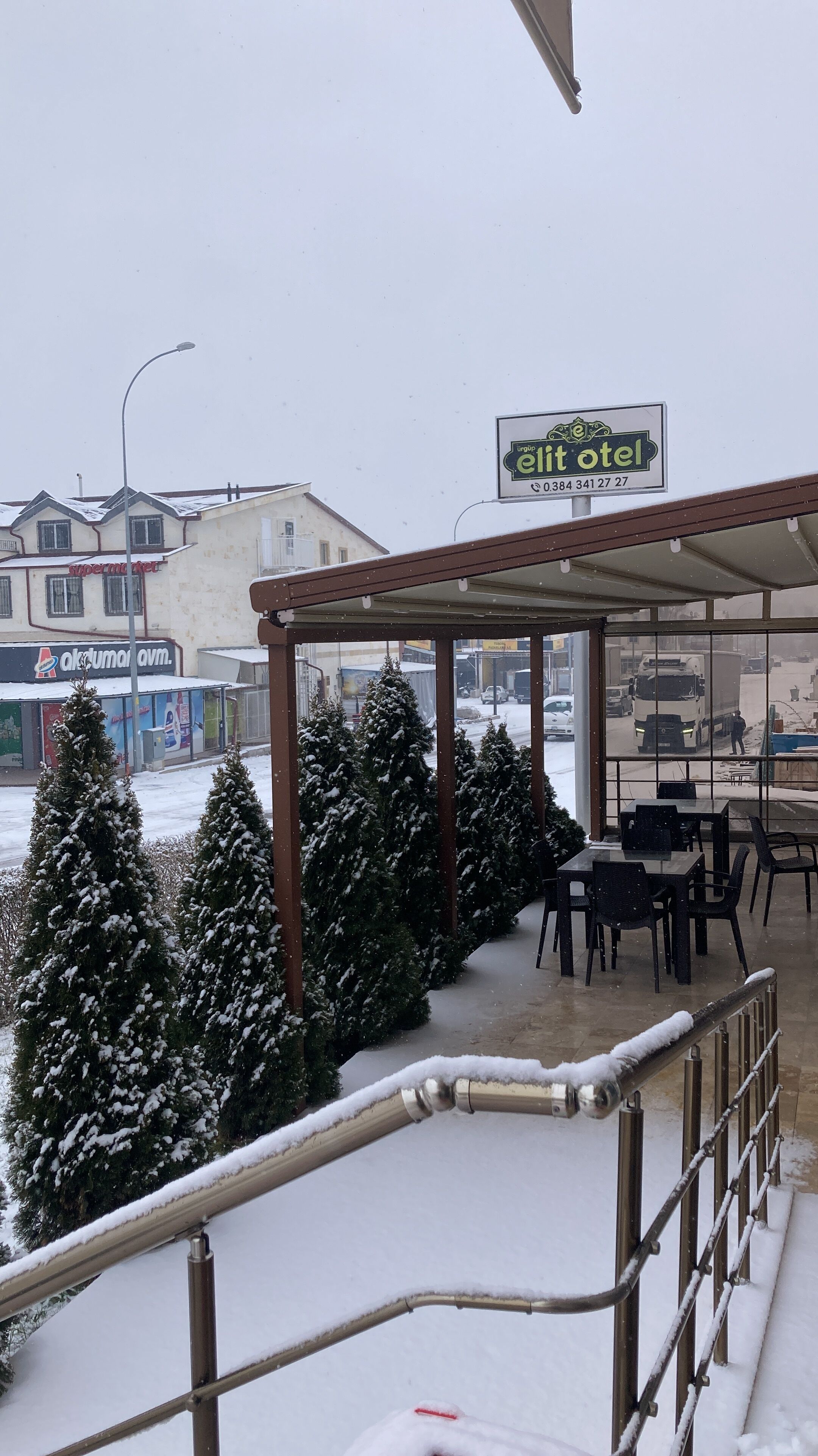 Una zona de estar al aire libre techada, con árboles cubiertos de nieve y un cartel que dice 'elit hotel'.