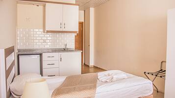 Habitación de hotel con cama, lámpara de noche, una kitchenette pequeña con lavamanos y un tendedero.