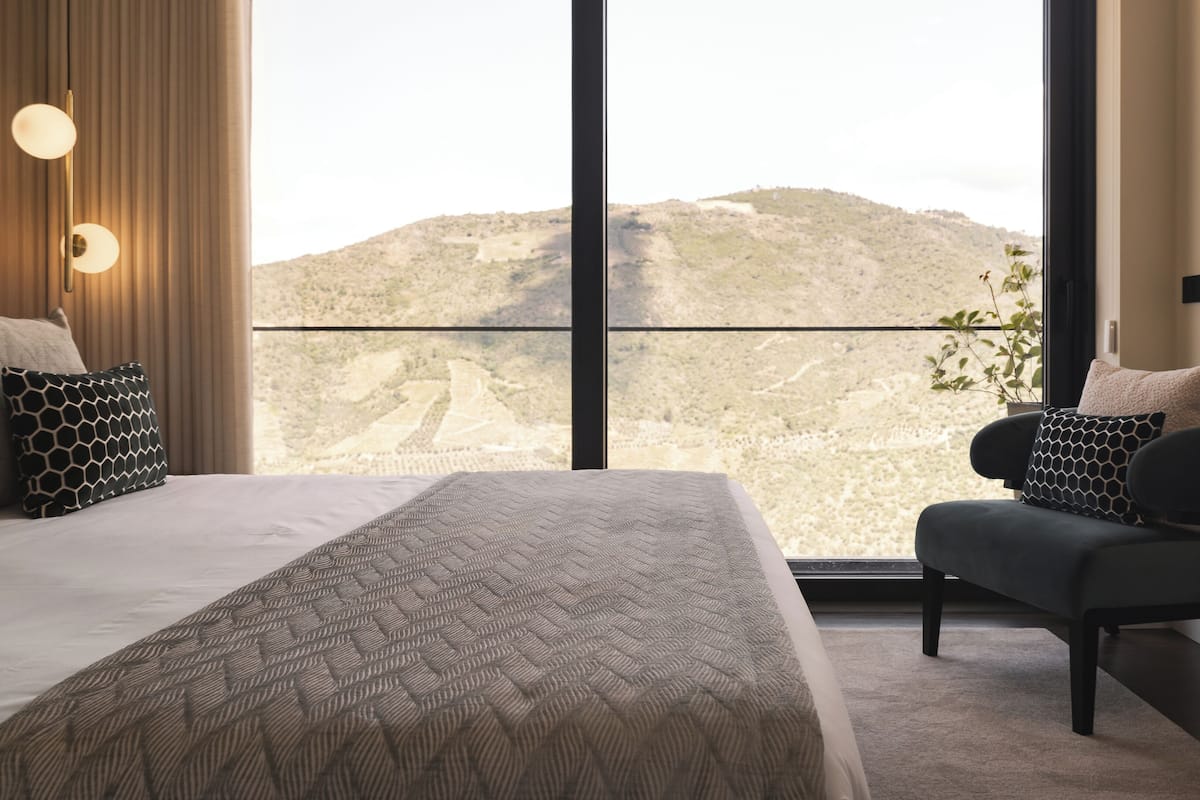 Ein Hotelzimmer mit einem großen Bett, einer Couch und Blick auf eine gebirgige Landschaft durch große Fenster.