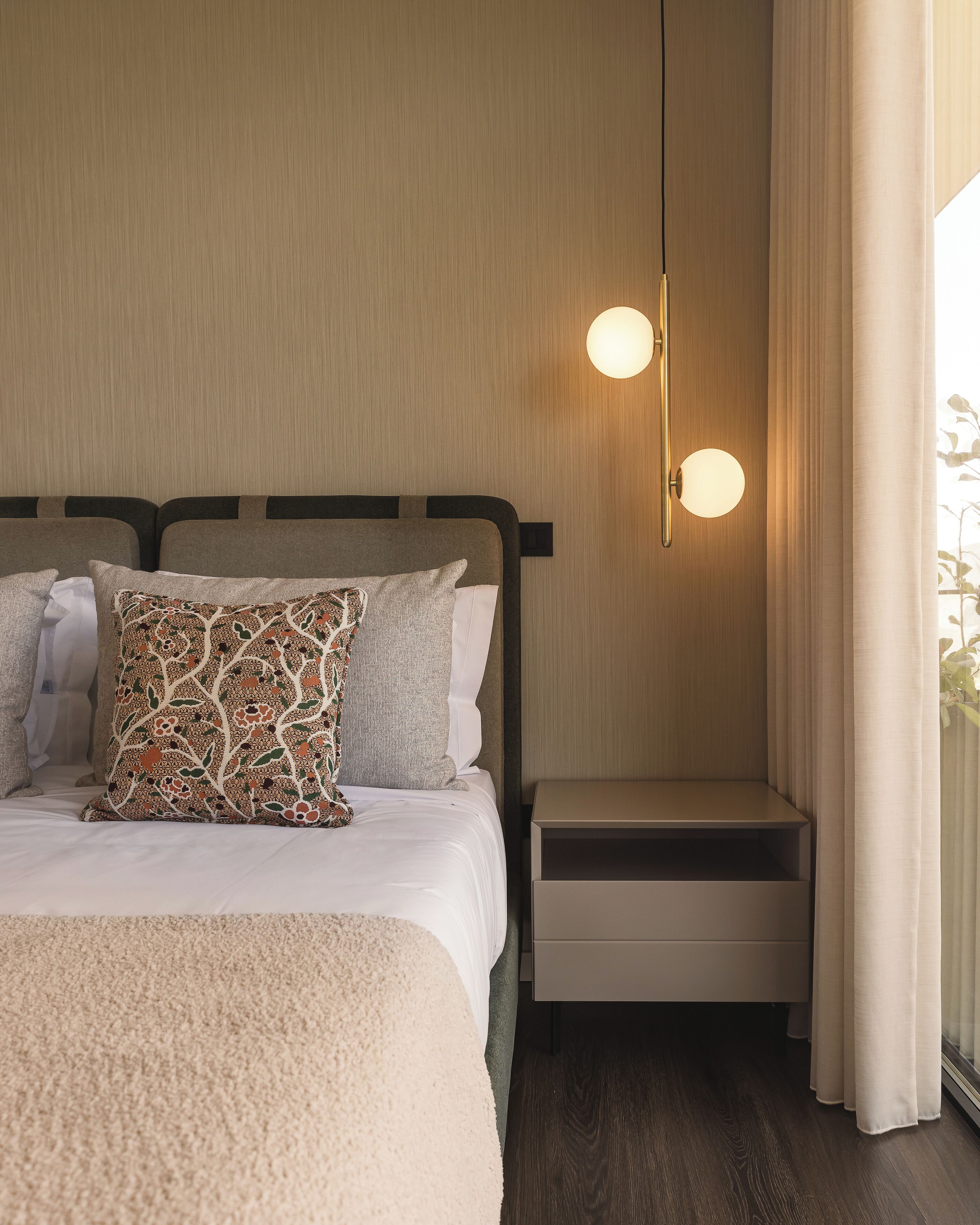 Una cama bien hecha con almohadas estampadas, una mesita de noche y una lámpara de pared.