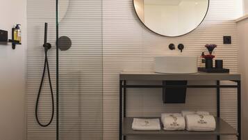 A modern bathroom with a shower, a round mirror, a sink with a white basin, and a shelf with towels.