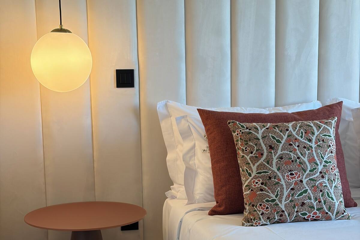 Ein Hotelzimmer mit einem Bett, einem Nachttisch, einer Hängelampe und einem an der Wand montierten Bedienfeld.