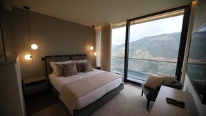 A modern hotel room with a large bed, a desk, and a view of a mountainous landscape. - Quinta Vale de Lobos Douro (Armamar)