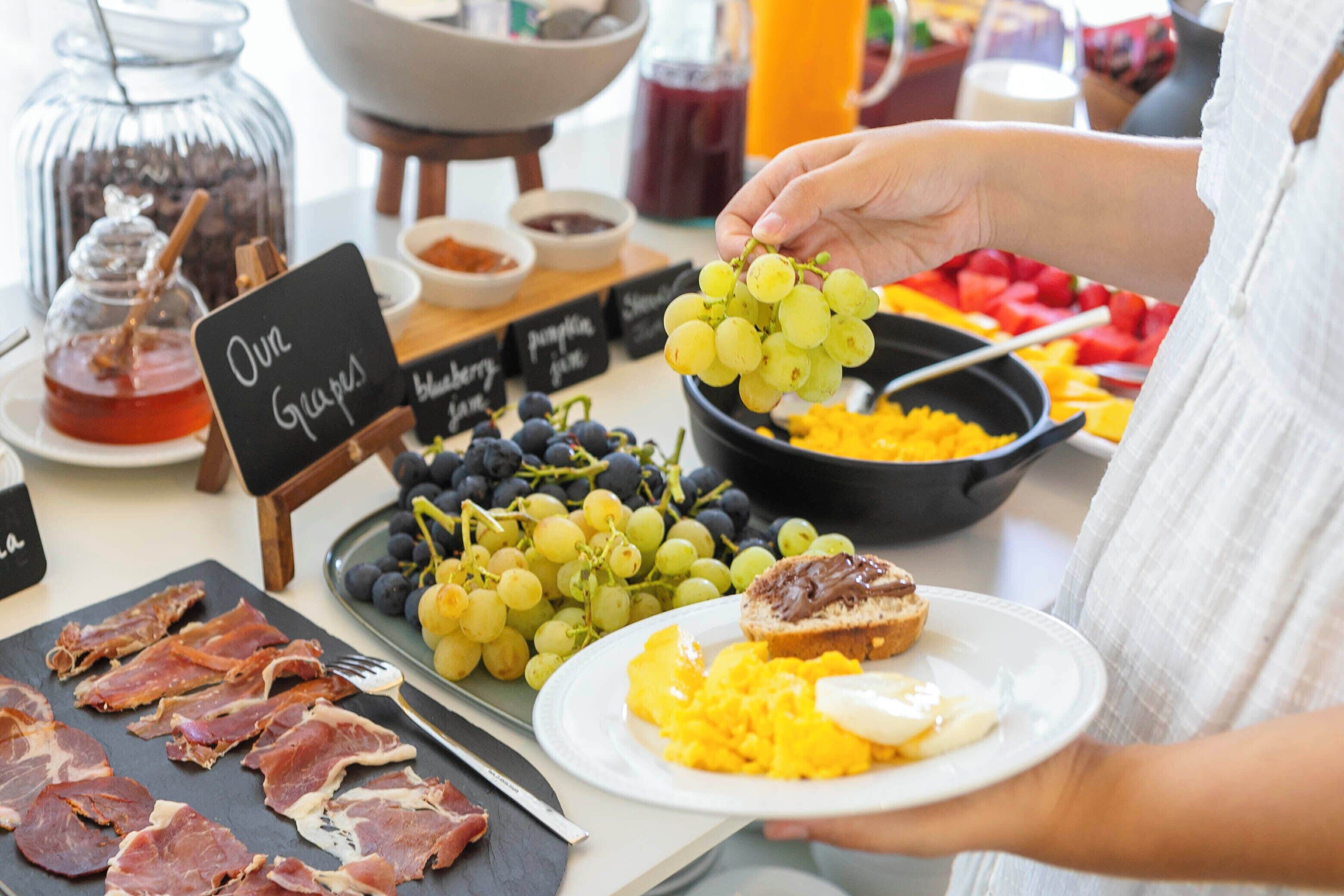 A breakfast buffet with various food items including grapes, eggs, and meats.